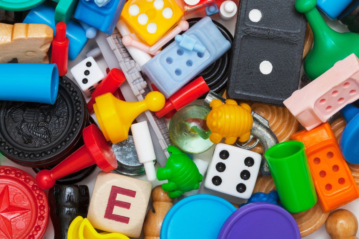 Das Bild zeigt bunte Spielfiguren und Würfel durcheinandergemischt.