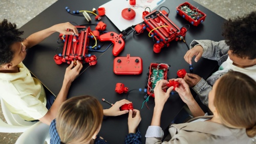 Kinder bauen mit einem Bausatz und Platinen, Kabeln, Leuchtdioden und Schaltern ein kleines, rotes Fahrzeug zusammen 