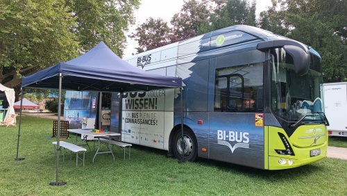 Das Bild zeigt den BI-BUS der Stadtbibliothek Saarbrücken, einen Bücherbus, der Grundschulen in Deutschland und Frankreich anfährt. Der Buch ist überwiegend blau mit Fantasy-Motiven und den Schriftzügen "Ein Bus voller Wissen", sowie "Un Bus plein de Conn