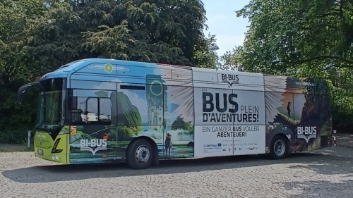 Der BI-BUS steht auf einem gepflasterten Platz vor mehreren Bäumen.