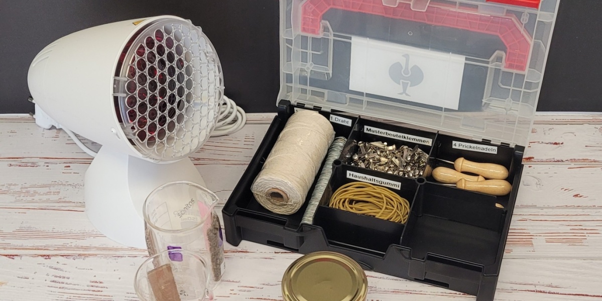 Das Bild zeigt den Inhalt der Erfindekiste mit einer Werkzeugbox, einer Lampe, Gläsern und weiteren verschiedenen Werkzeugen wie Schere und Zangen.